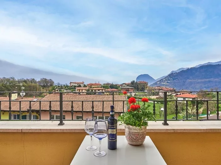 bergen en daken vanaf balkon waar tafel met twee wijglazen en fles wijn op staat